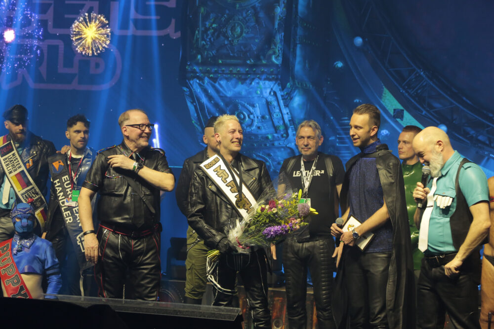 Mr Fetish World 2025 holding flowers on stage during Darklands 2025.