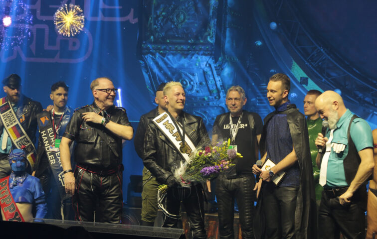 Mr Fetish World 2025 holding flowers on stage during Darklands 2025.